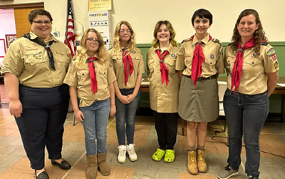 Four female scouts and two female leaders in uniform at a Court of Honor ceremony