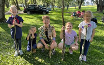 Male scout with female cub scouts in a park holding walking sticks