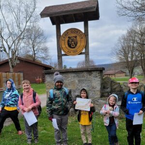 6 Cub Scout boy and girl members with maps in front of the sign for Camp Gorton