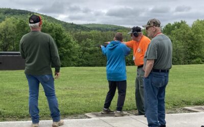 A Scout learns to shoot clay pigeons with a shotgun while instructor and three others look on