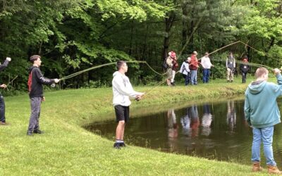 Four Scouts practice fly casting into a pond. In the background, another group of Scouts learns about reel casting,