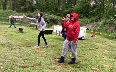 Two female Scouts throw tomahawks while being watched by an adult volunteer