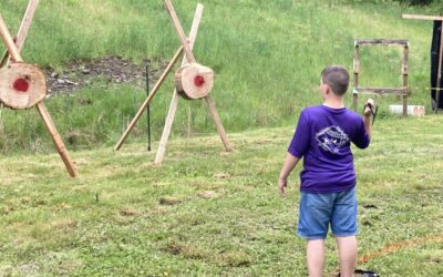 Two male Scouts throwing tomahawks at round targets while being watched by an adult volunteer